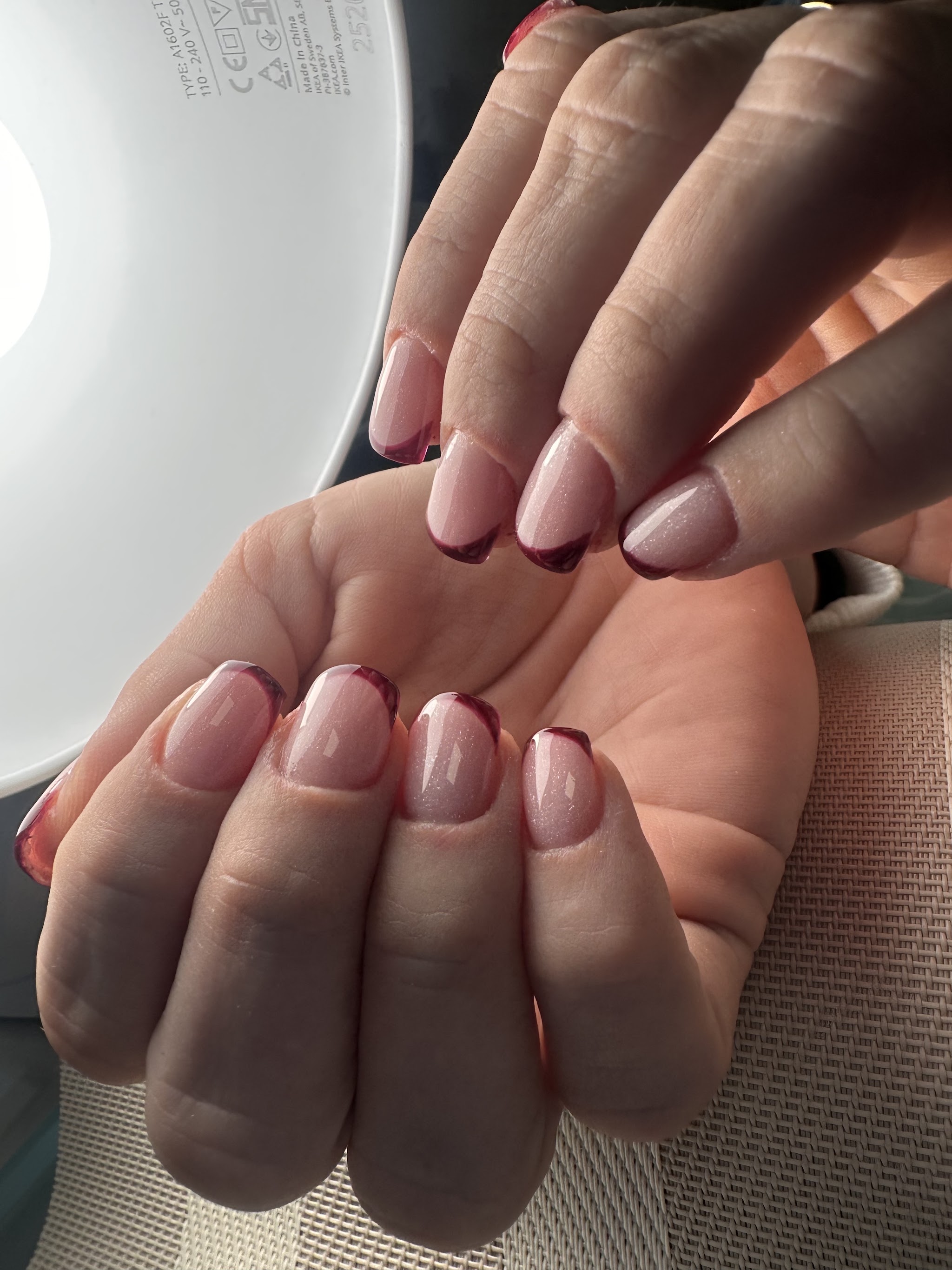Korte French nagels met donkerrode tips onder de lamp